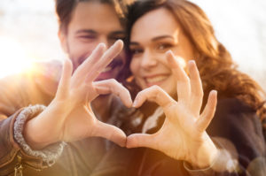 couple in healthy relationship smiling and making heart with their hands