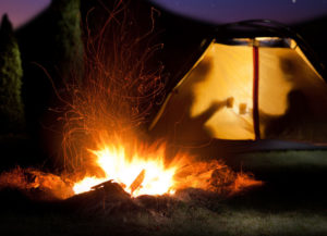 Couple camping that understands how to get more romance in your relationship, dark outside with fire blazing and couple in a tent, shadows of a couple drinking out of mugs